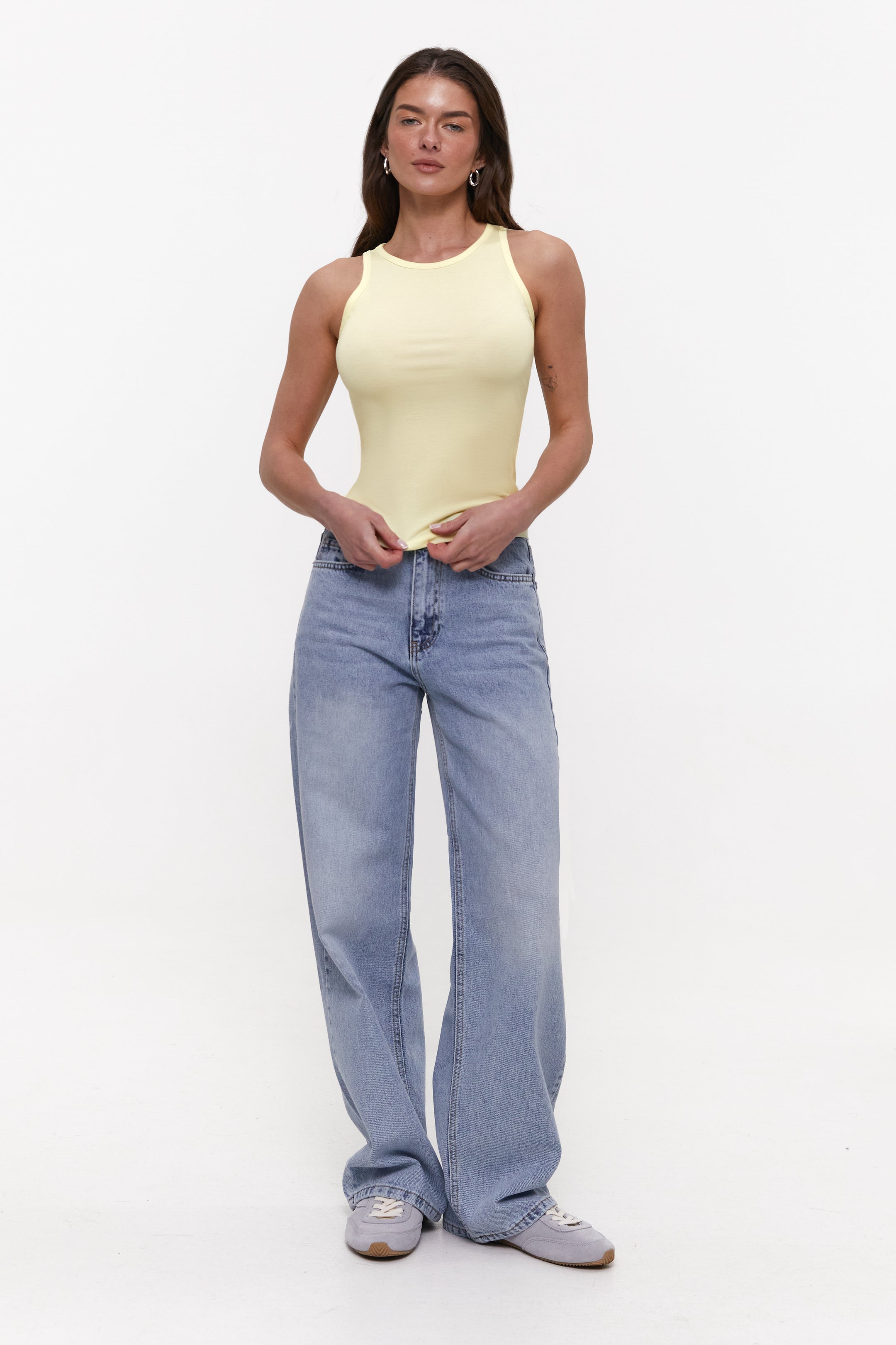 Woman wearing a yellow tank top and blue jeans on a white background