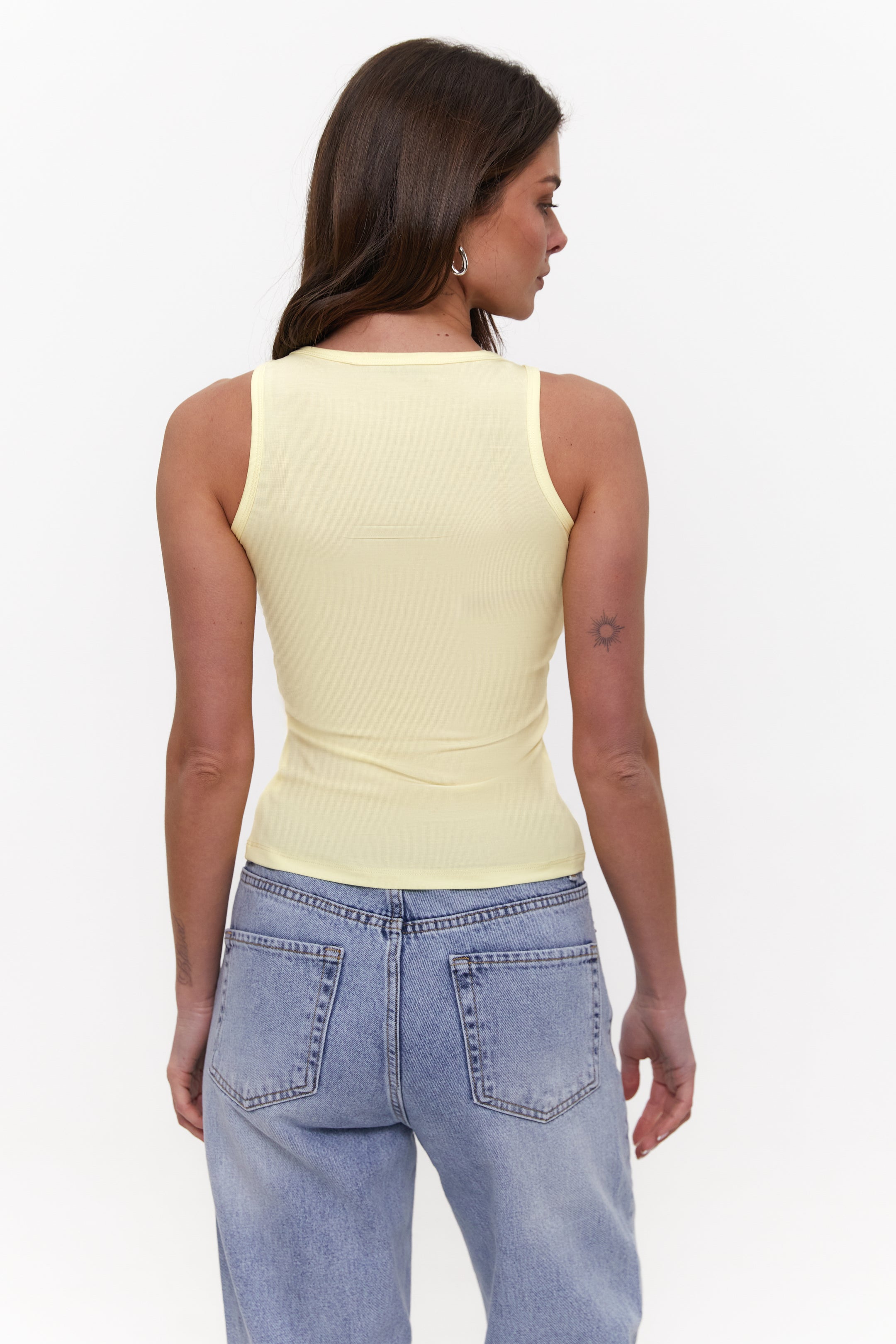 Woman wearing a yellow tank top and blue jeans on a white background